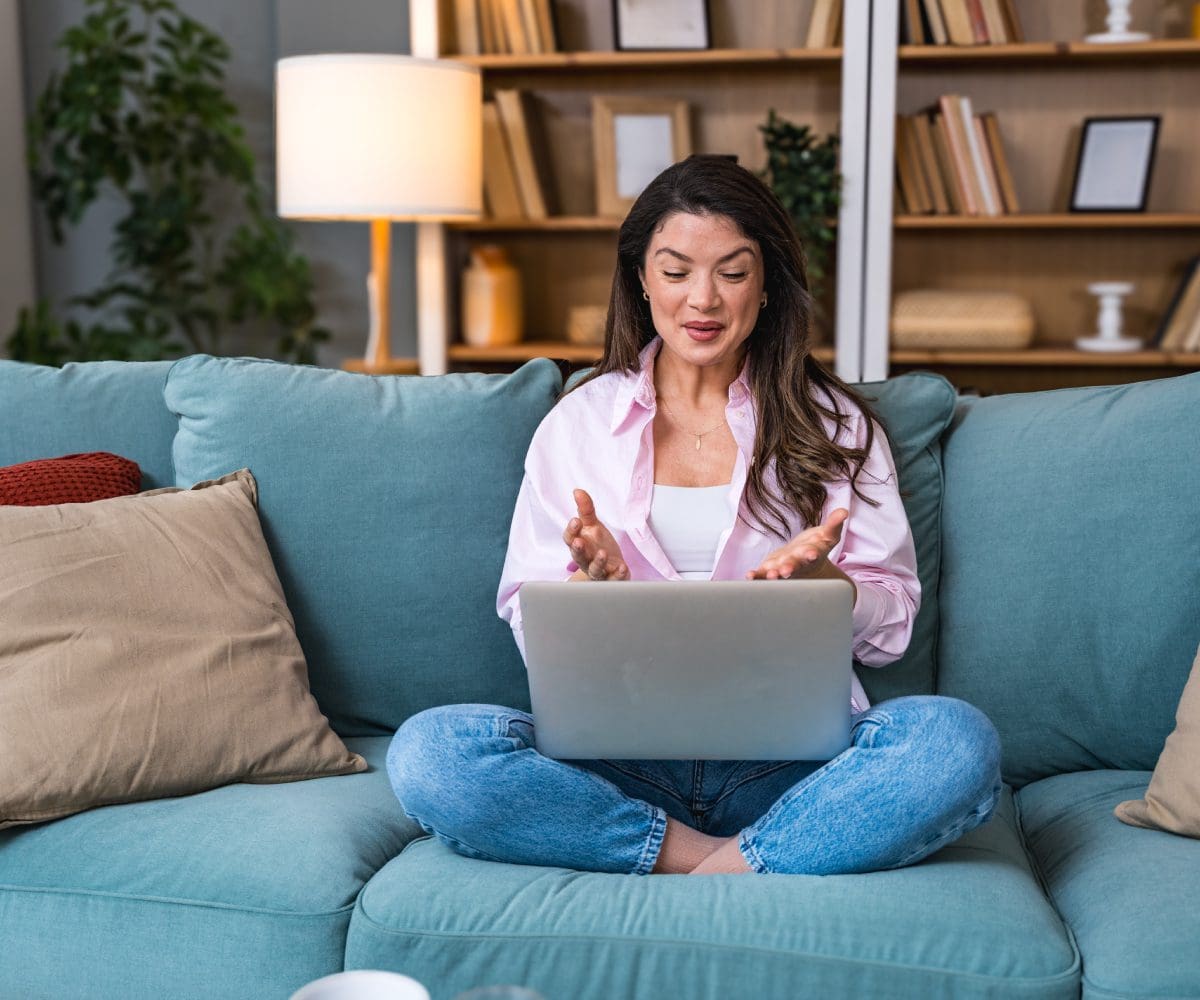 Woman sitting cross-legged on couch using laptop.