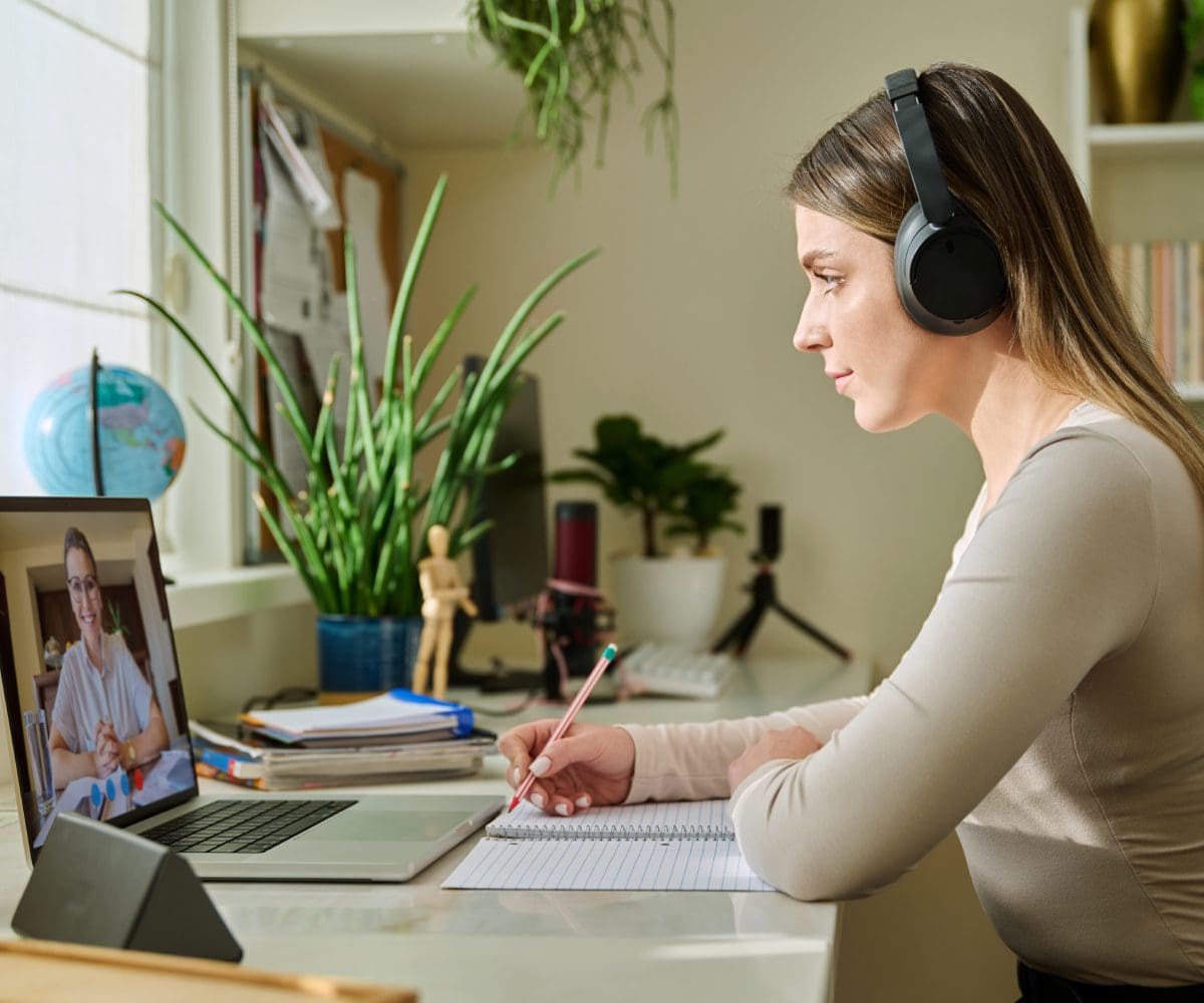 Woman wearing headphones studying with a laptop and notebook.